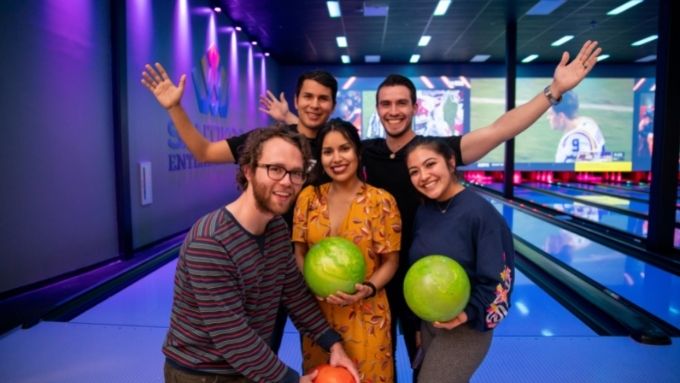 Group of adults posing in front of bowling alley holding bowling balls
